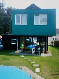 Türkisfarbener Hausaufbau vor Wiese und Pool